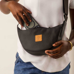 Black round mini vegan leather shoulder bag by Ecodunia with Kenyan fabric lining, featuring a compact design and adjustable strap.