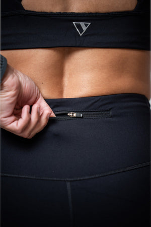 Hot Trend Vault women's black three-quarter length technical leggings, close-up of fabric and fit in a stylish workout pose.